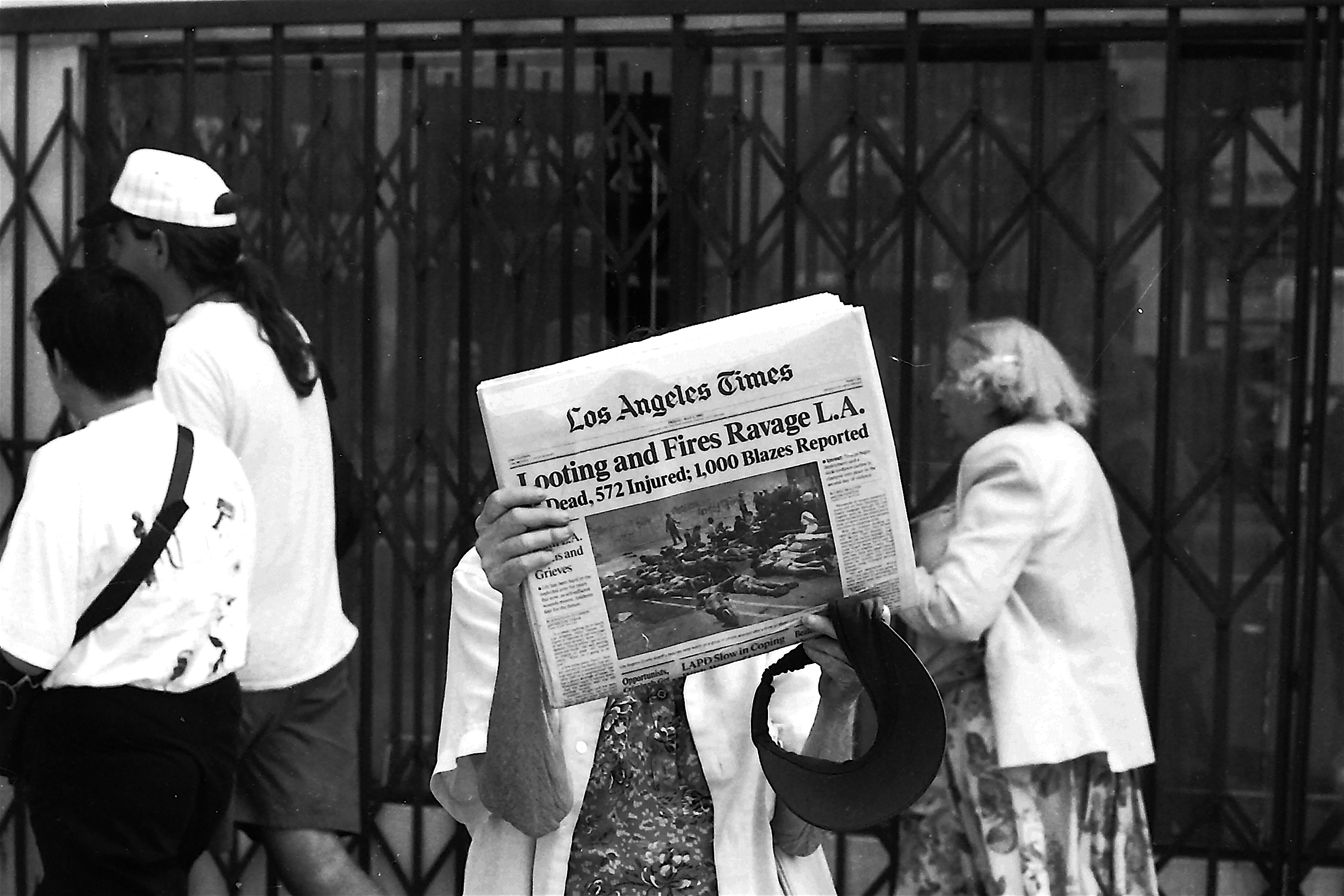 Woman holds newspaper up to show headline, "looting and fires ravage L.A."