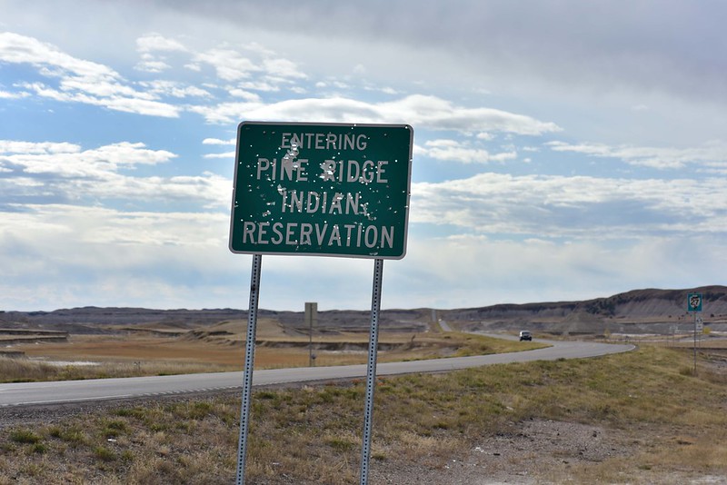 Landscape color photo of the Pine Ridge road sign, covered in bullet holes.